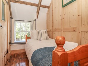 A bedroom with a wooden ceiling, a window, a bed with a headboard, and a wooden floor.