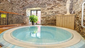 Une piscine intérieure aux murs en pierre, dotée d’une terrasse en bois et agrémentée d’une plante en pot.