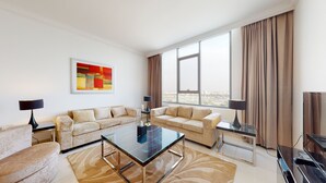 Una sala de estar moderna con dos sofás color beige, una mesa de centro de vidrio y un amplio ventanal con cortinas.