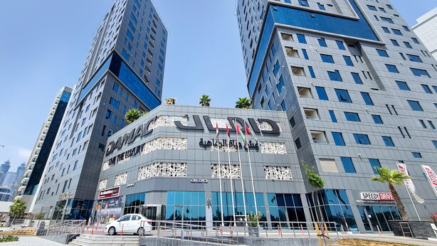 Un edificio moderno con un llamativo letrero 'JIND', varios pisos y un anuncio de 'Speedy Drive'.