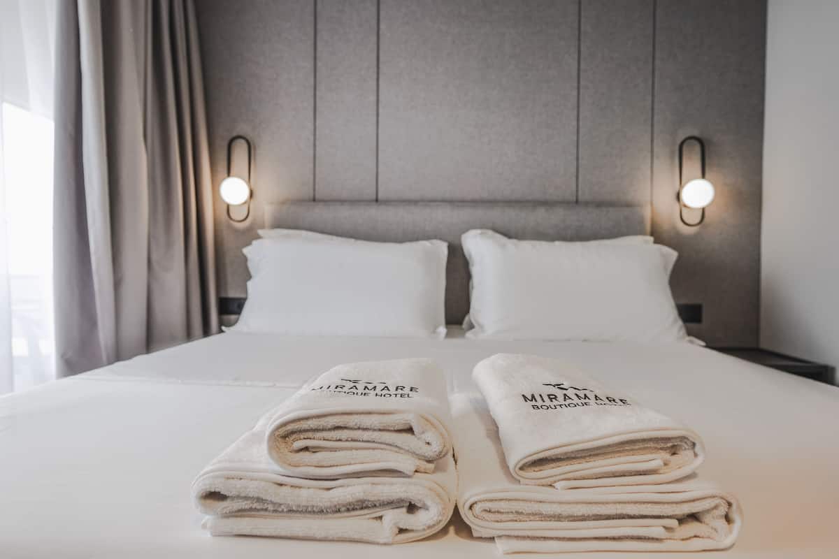 Een net opgemaakt bed met twee kussens en twee gevouwen handdoeken met tekst erop.
