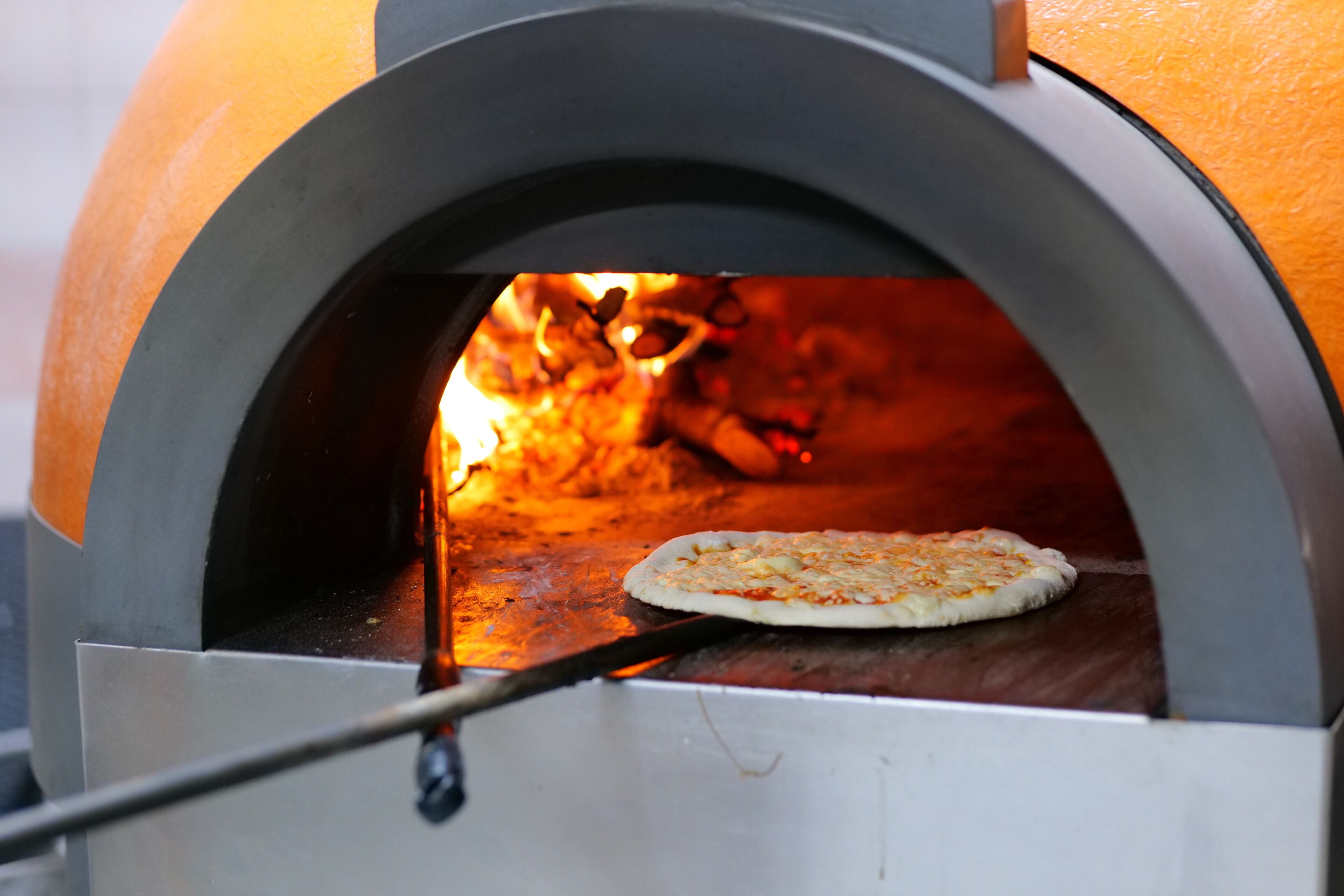 A pizza oven with a pizza inside, a fire burning beneath, and a metal tool in front.
