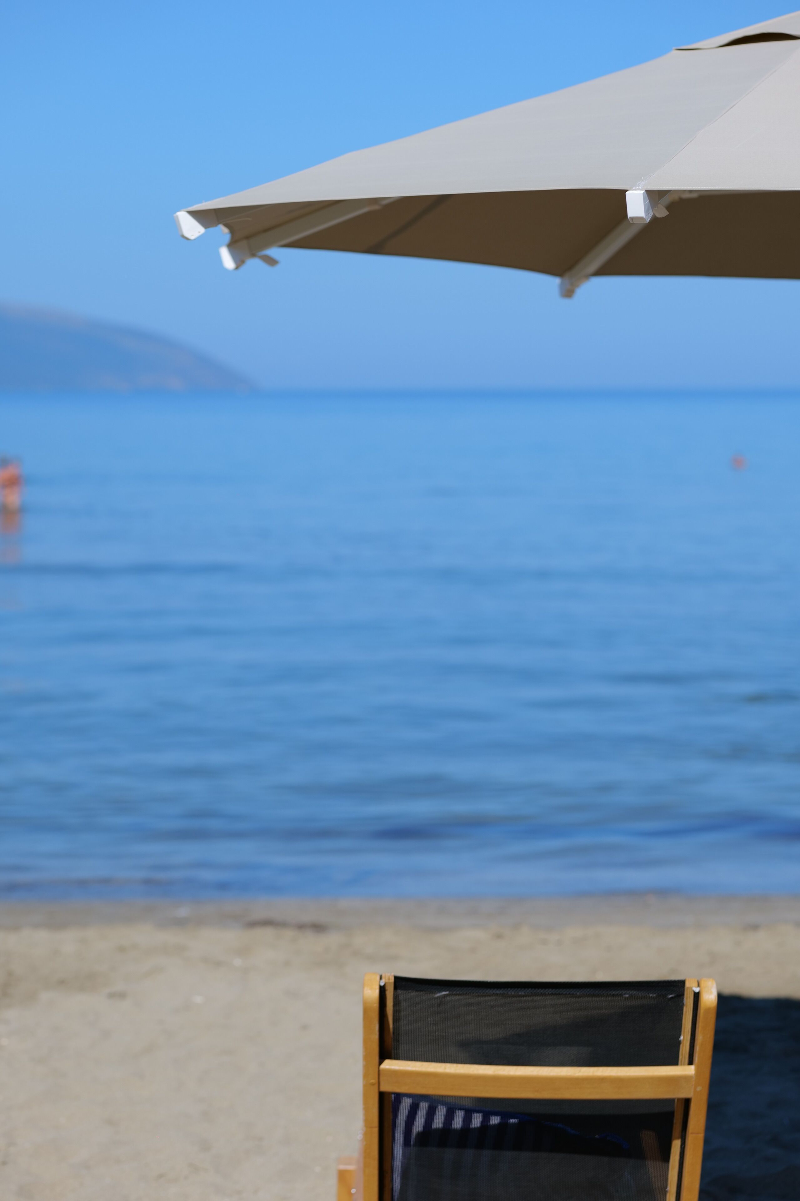 A beach chair under a beach umbrella with a view of the ocean and a distant mountain.