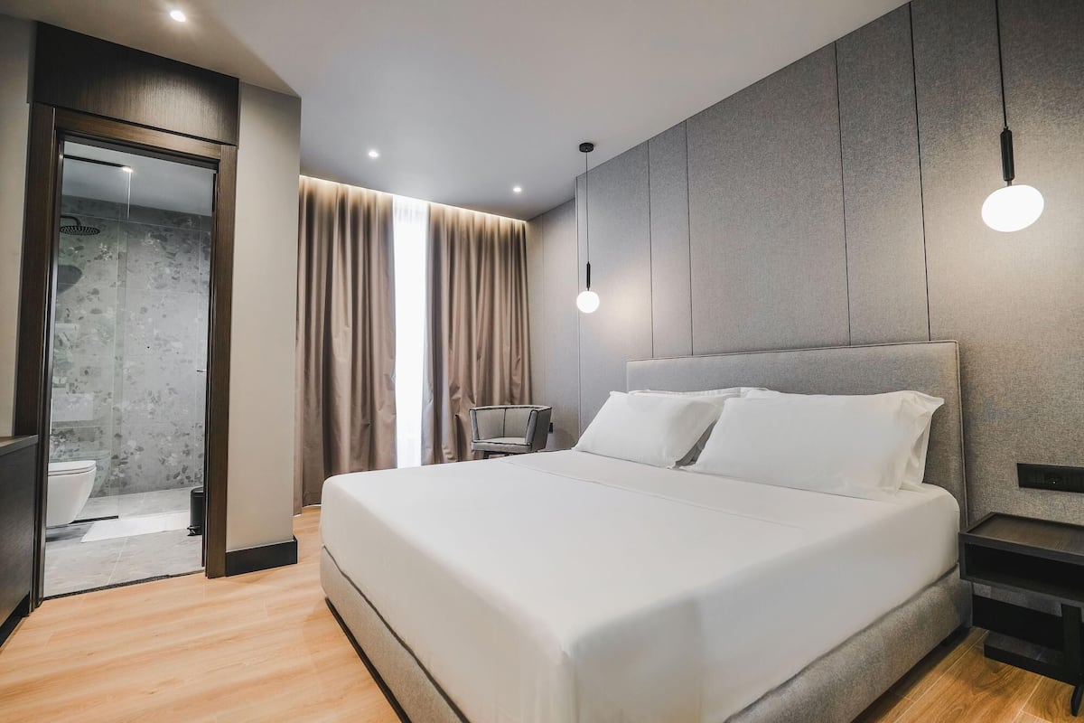 Een moderne hotelkamer met een groot bed, een zithoek met een stoel, een televisie en uitzicht op de badkamer.