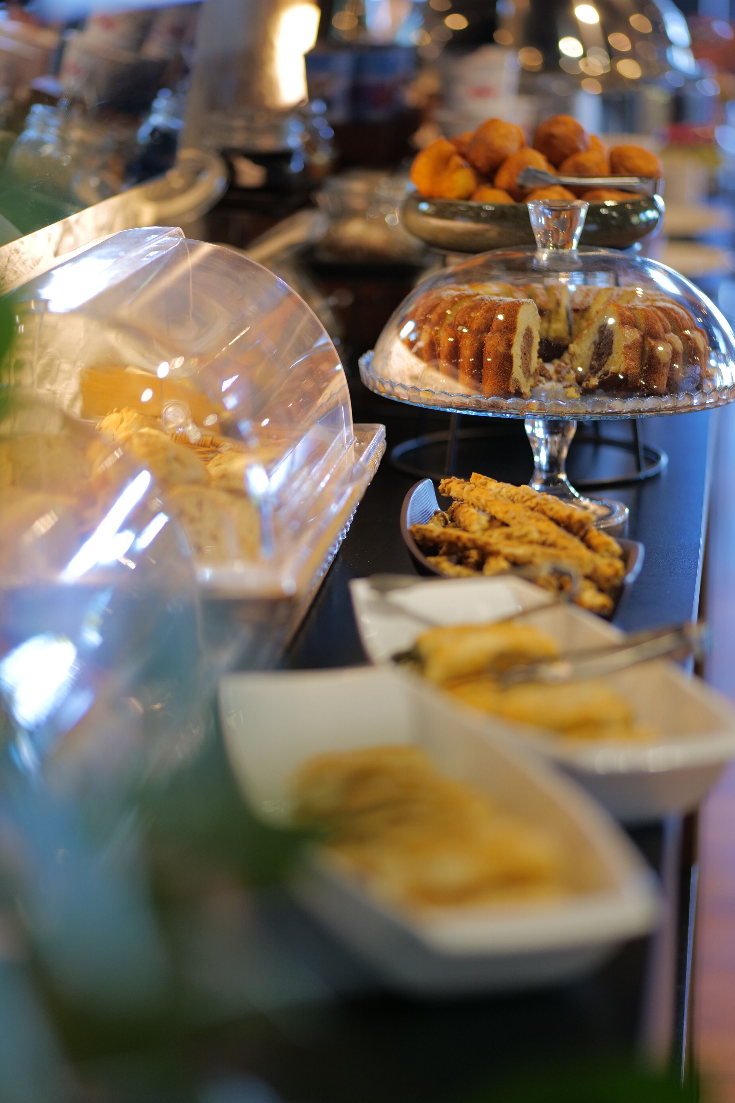 Ein Buffet mit verschiedenen Speisen, darunter Gebäck und frittierte Speisen, präsentiert in klaren Behältern.