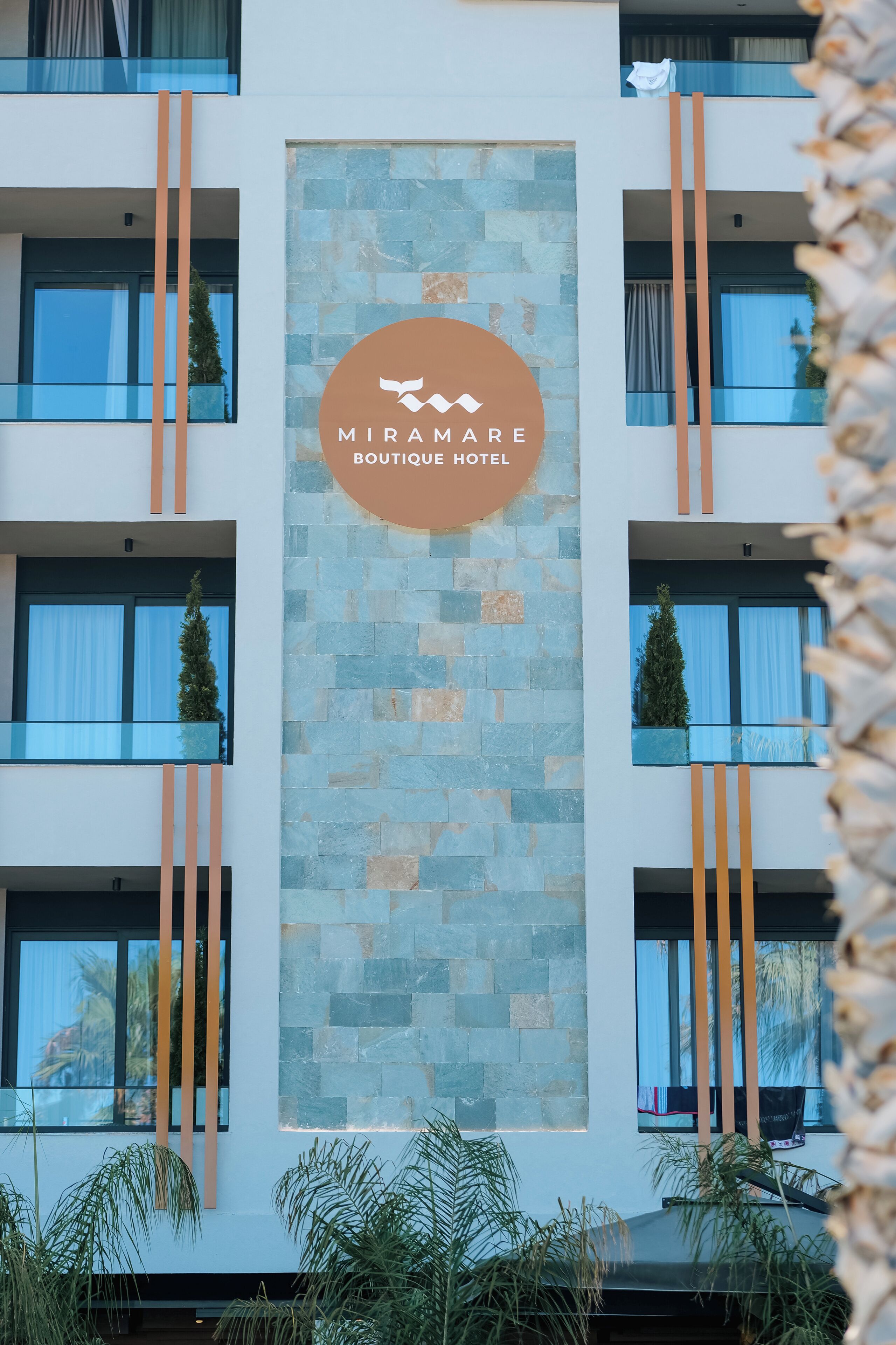 Een moderne hotelgevel met een logo, balkons en stenen accenten.