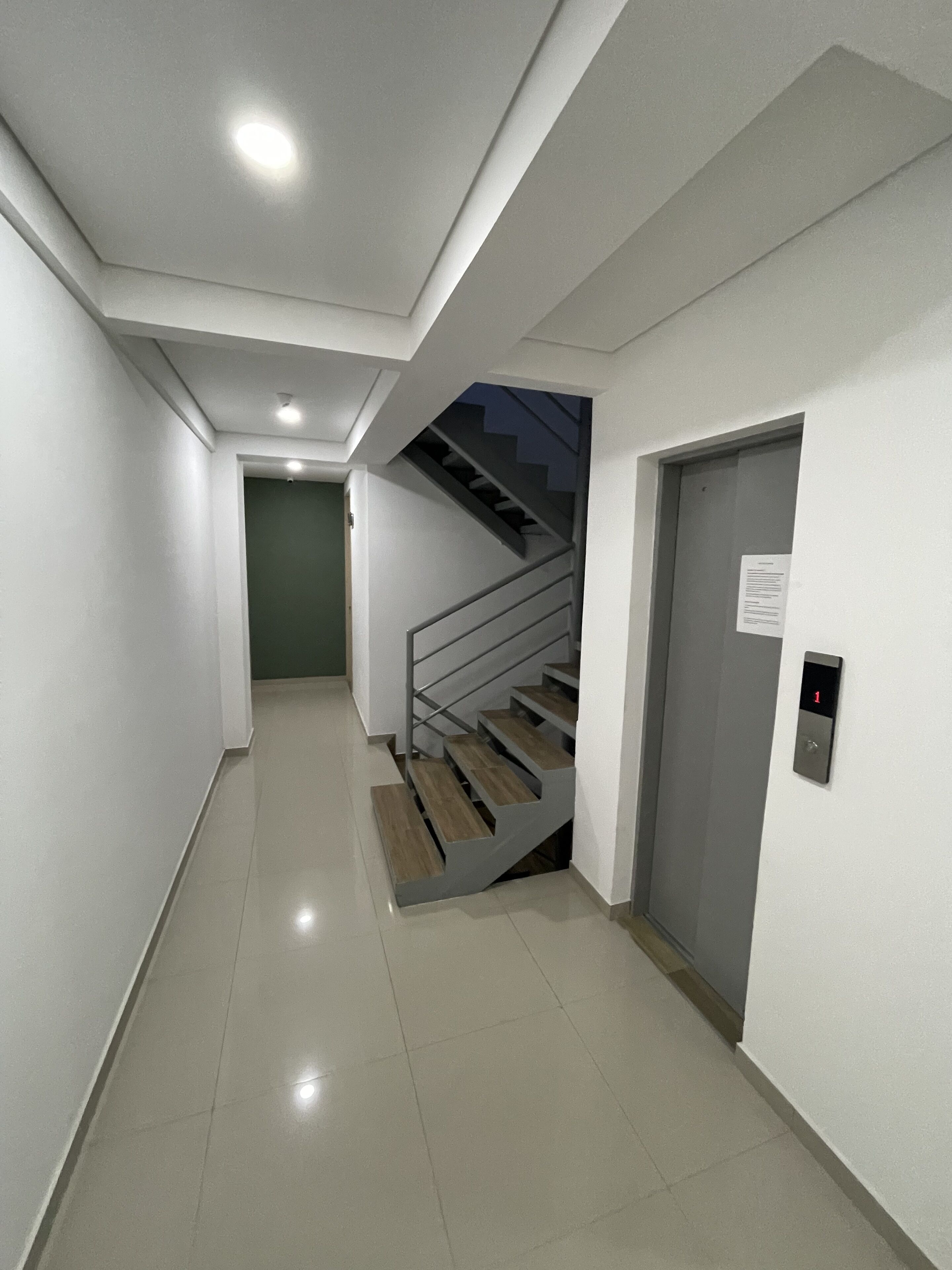 A modern hallway with a staircase, a door with an elevator button, and a ceiling light.