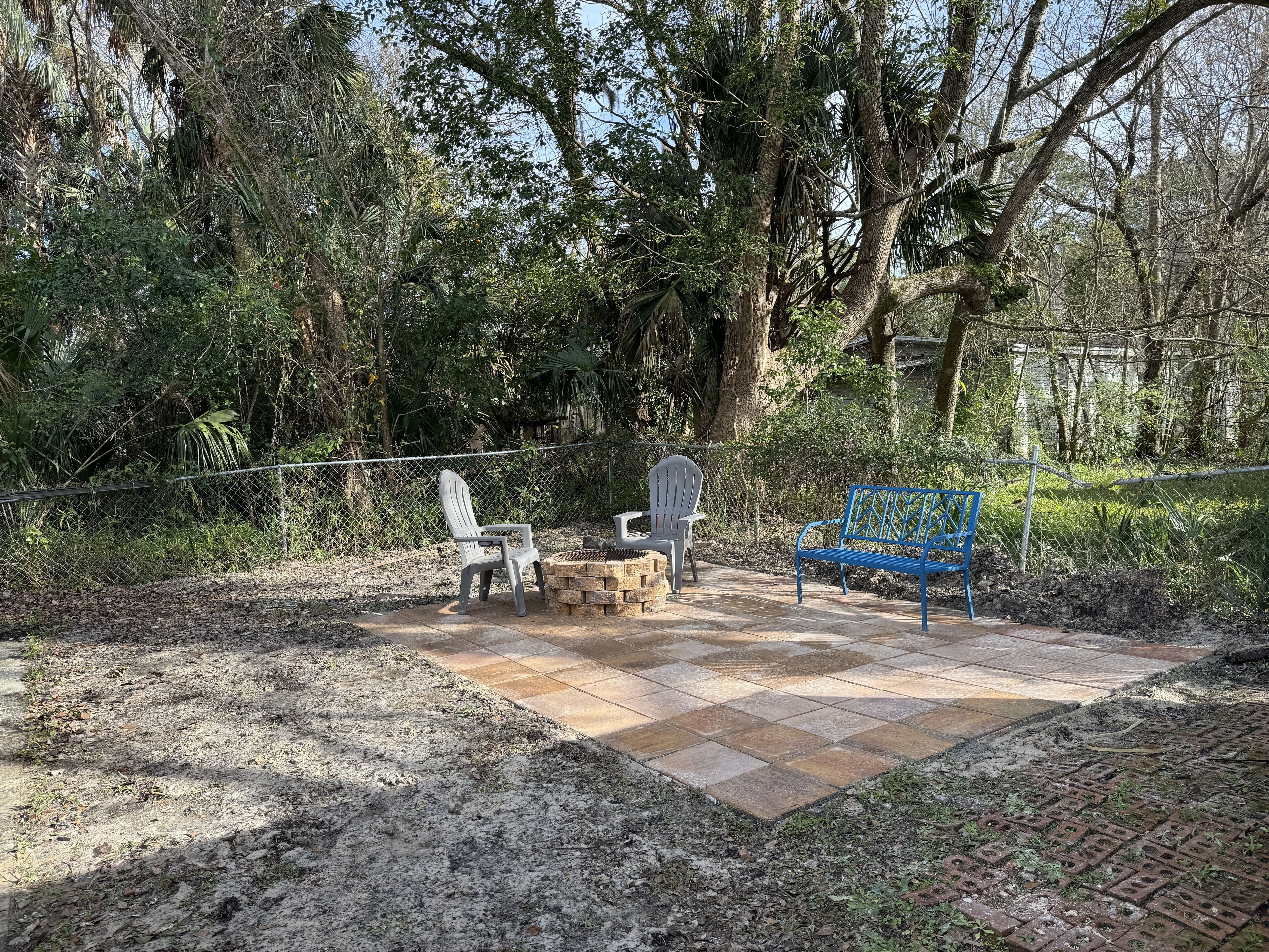 Un espace patio doté d’un sol carrelé en pierre, de deux fauteuils Adirondack et d’un banc en métal bleu.