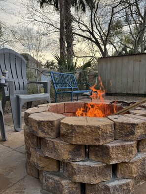 A stone fire pit with a blue metal bench and a grey plastic chair nearby.