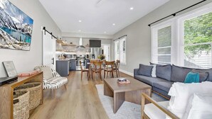 Een ruime woonkamer met een bank, salontafel en eettafel. Achtergrond is een keuken met moderne apparatuur.