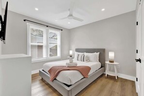 Un dormitorio moderno con cama, mesitas de noche, ventilador de techo y ventana con persianas.