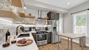 Een moderne keuken met een centraal eiland, roestvrijstalen apparatuur en houten planken.