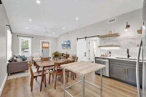 A modern kitchen with a dining area, wooden flooring, and a view of the outdoors.