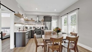 Een moderne keuken met een centraal eiland, inbouwapparatuur en een eethoek met houten stoelen.