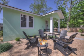 A house with a green exterior, a porch with Adirondack chairs, and a table with a beverage and snacks.
