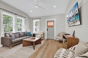 Un salon spacieux avec un canapé, une table basse et des fauteuils, de grandes fenêtres et un tableau accroché au mur.
