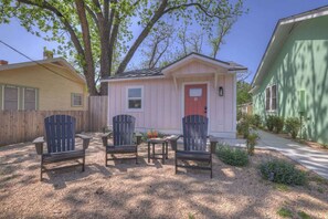 A small pink house with a red door, two Adirondack chairs, and a table in front.