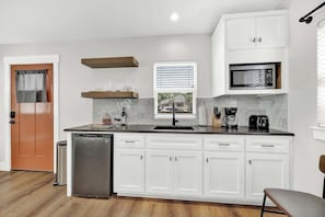 A modern kitchen with white cabinets, a black countertop, a built-in microwave, and a window with blinds.