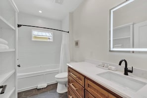 Une salle de bain moderne équipée d’une baignoire, de toilettes, d’un meuble-lavabo avec des tiroirs et d’un grand miroir.