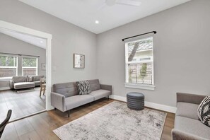 Ein modernes Wohnzimmer mit einem grauen Sofa, einem grauen Hocker und einem gemusterten Teppich.