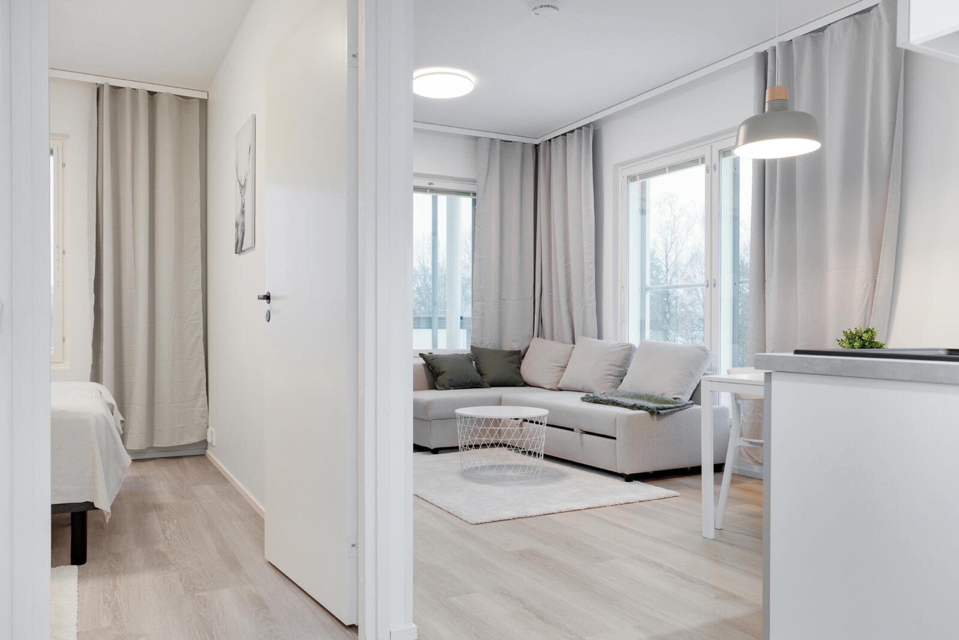Una sala de estar moderna y luminosa, con un sofá, una mesa de centro redonda y un comedor con una mesa y sillas blancas.