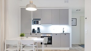 A modern kitchen with grey cabinets, a microwave, a coffee maker, and a sink. There is a dining table with white chairs and a small plant on it. - Forenom Serviced Apts Espoo Saunalahti (Espoo)