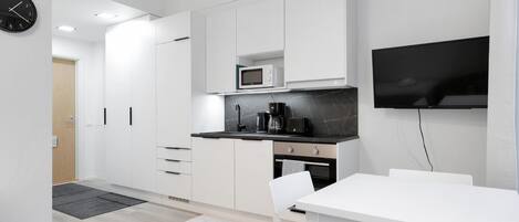 Una cocina moderna con armarios blancos, microondas, cafetera y un televisor de pantalla plana montado en la pared.