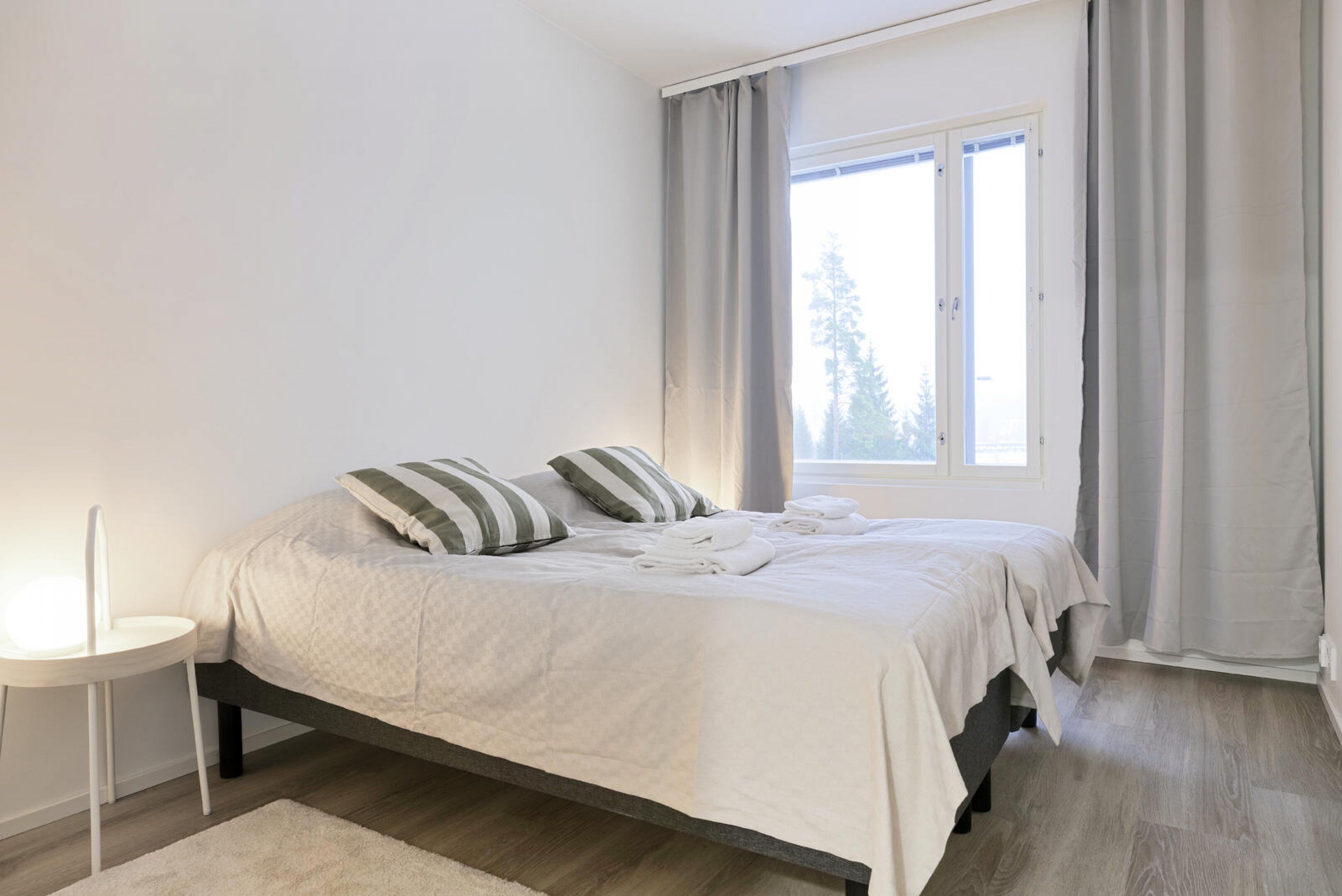 Una cama bien hecha con almohadas, una mesita de noche y una ventana con cortinas.