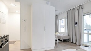 A modern hotel room with a large wardrobe, a bed with a white headboard, a small table, and a window with curtains. - Forenom Serviced Apts Espoo Saunalahti (Espoo)
