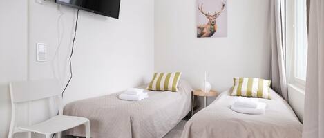 A hotel room with two beds, a TV mounted on the wall, a painting of a deer, and a white chair.