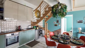 Una cocina moderna con una escalera de madera, un comedor con sillas rojas y una pared verde azulado.