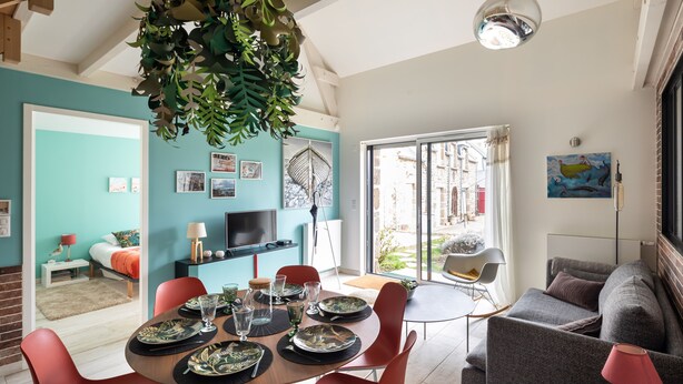 Una sala de estar moderna con comedor, sofá y televisor. Hay un ventanal con vistas al exterior.