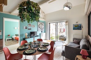 Ein modernes Wohnzimmer mit Essbereich, einer Couch und einem Fernseher. Ein großes Fenster bietet Blick ins Freie.