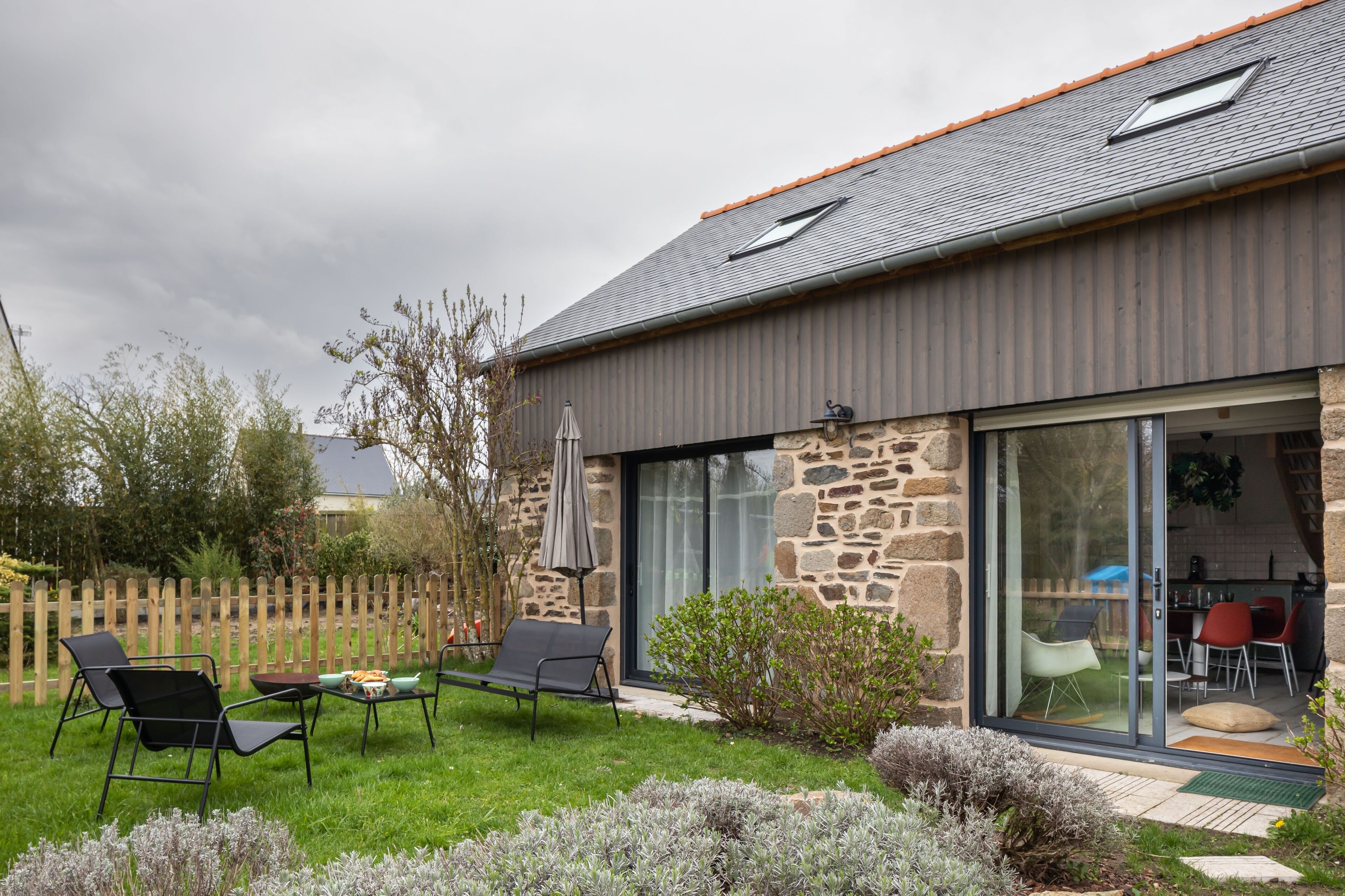 Een modern huis met een gevel van natuursteen, een grote schuifdeur en een terras met buitenmeubilair.