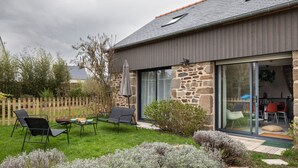 Una casa moderna con fachada de piedra, un amplio ventanal corredero y un patio con mobiliario exterior.