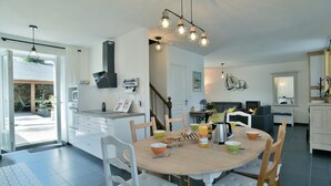 Moderni keittiö, jossa on ruokailutila. Keittiössä on suuri keittiösaareke, valkoiset kaapit ja riippuvalaisin.