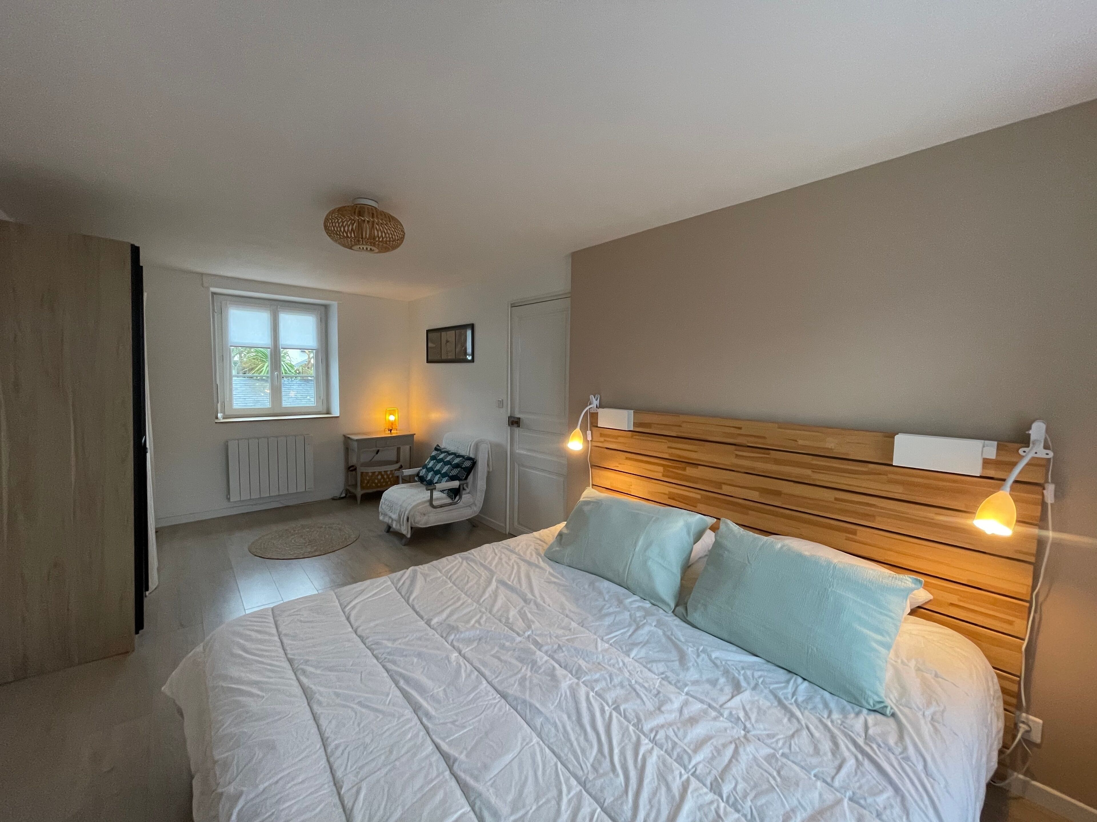 Een slaapkamer met een groot bed, nachtlampjes, een stoel, een raam en een radiator.