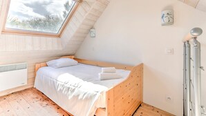 A bedroom with a sloped ceiling, a skylight, a bed, a wall-mounted clock, and a radiator. - Maison des Goelands - 50m de la plage (Pléneuf-Val-André)