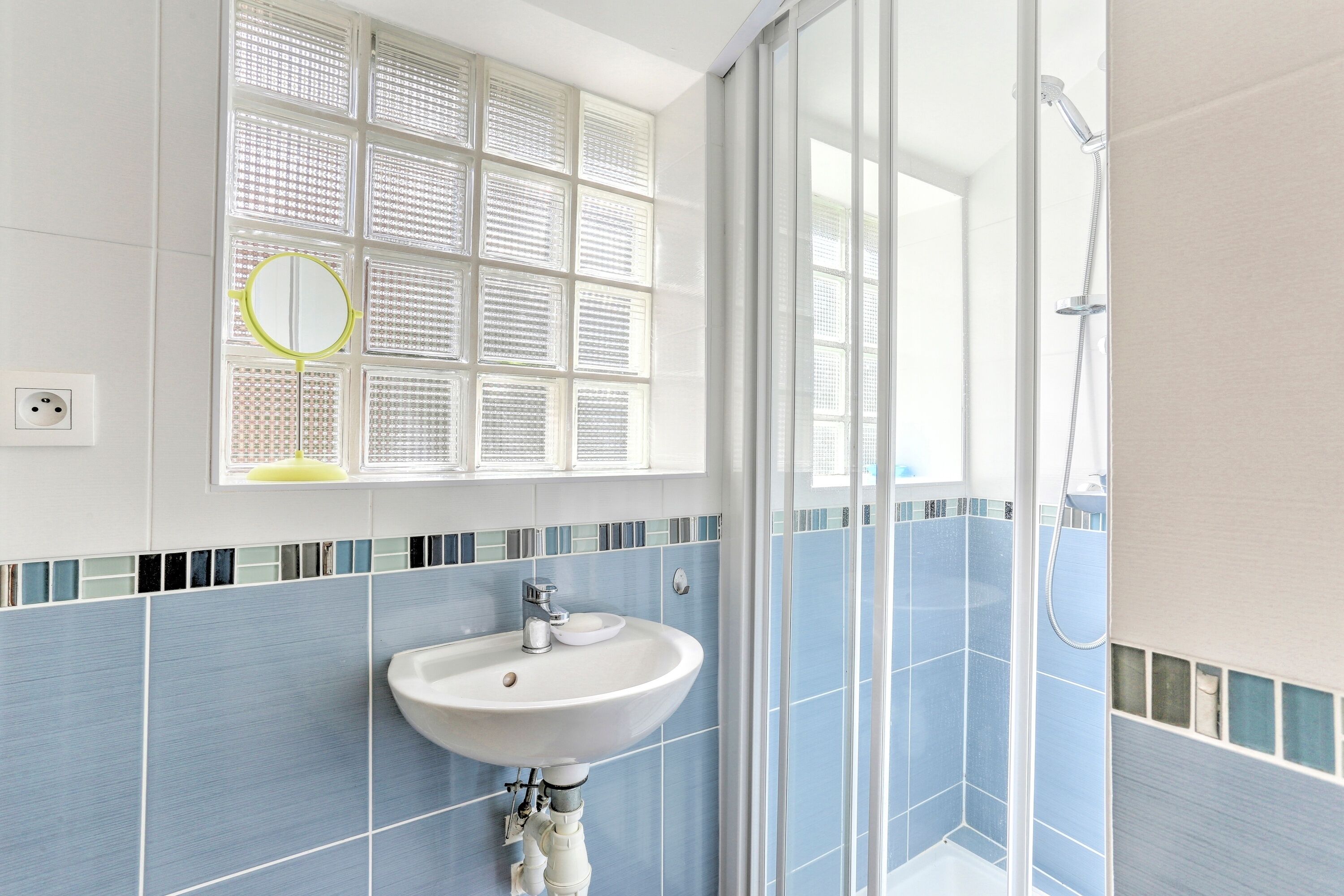 A bathroom with a sink, mirror, and shower.
