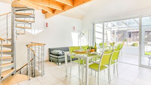 A modern interior with a spiral staircase, a dining area with green chairs, and a large glass door leading outside. - Maison des Goelands - 50m de la plage (Pléneuf-Val-André)