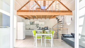 A modern kitchen with white cabinets, a dining table with four chairs, and a staircase leading to a loft area. - Maison des Goelands - 50m de la plage (Pléneuf-Val-André)
