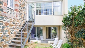 A two-story house with a stone facade, a glass conservatory, and a patio with outdoor seating. - Maison des Goelands - 50m de la plage (Pléneuf-Val-André)