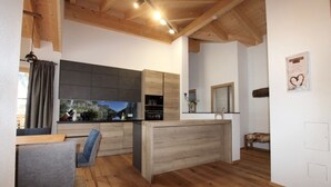 Une cuisine moderne avec des meubles en bois, un coin repas avec une chaise grise et un plafond en bois.