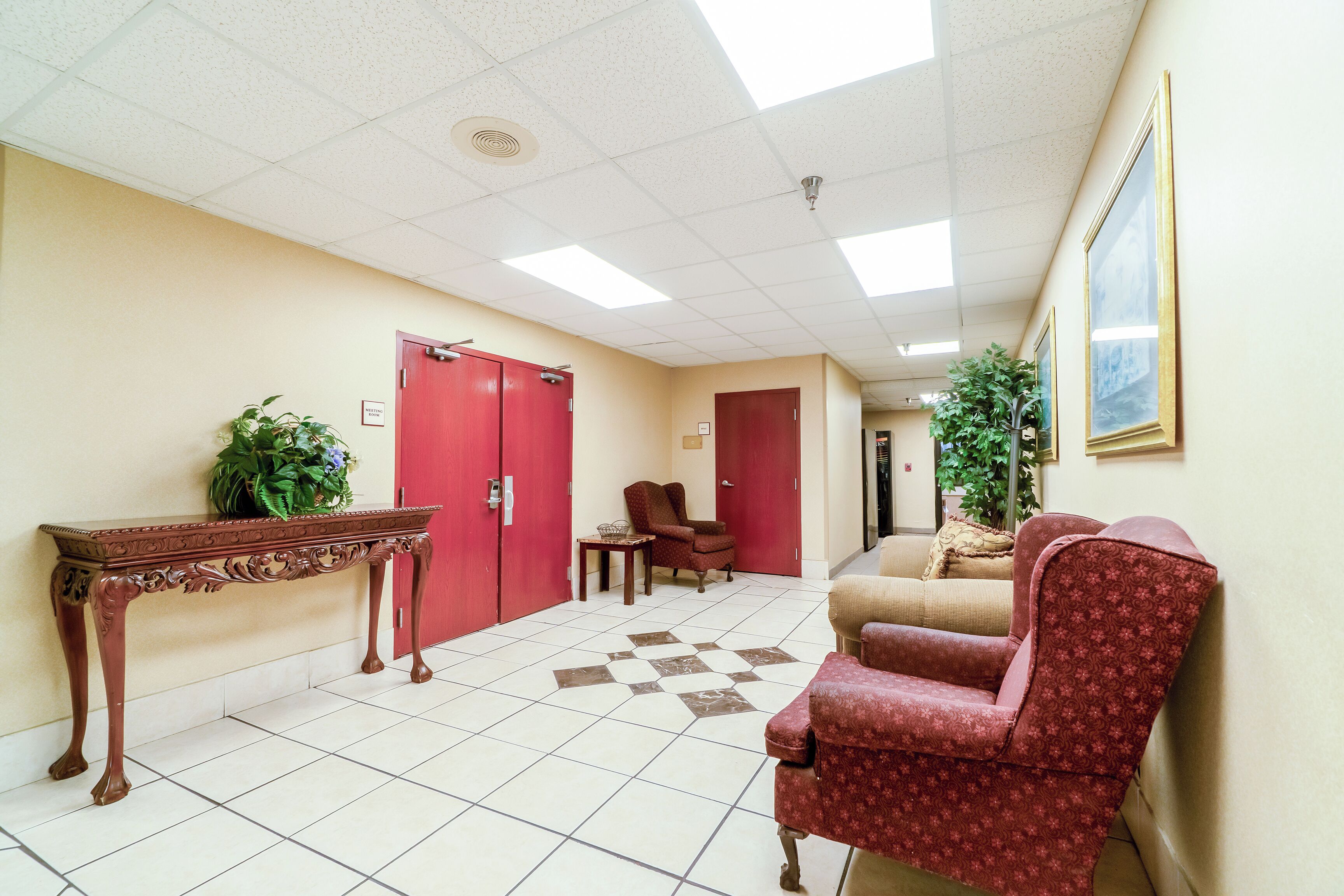Un couloir avec une porte rouge, une table sur laquelle est posée une plante, un tapis à motifs et un fauteuil rouge.
