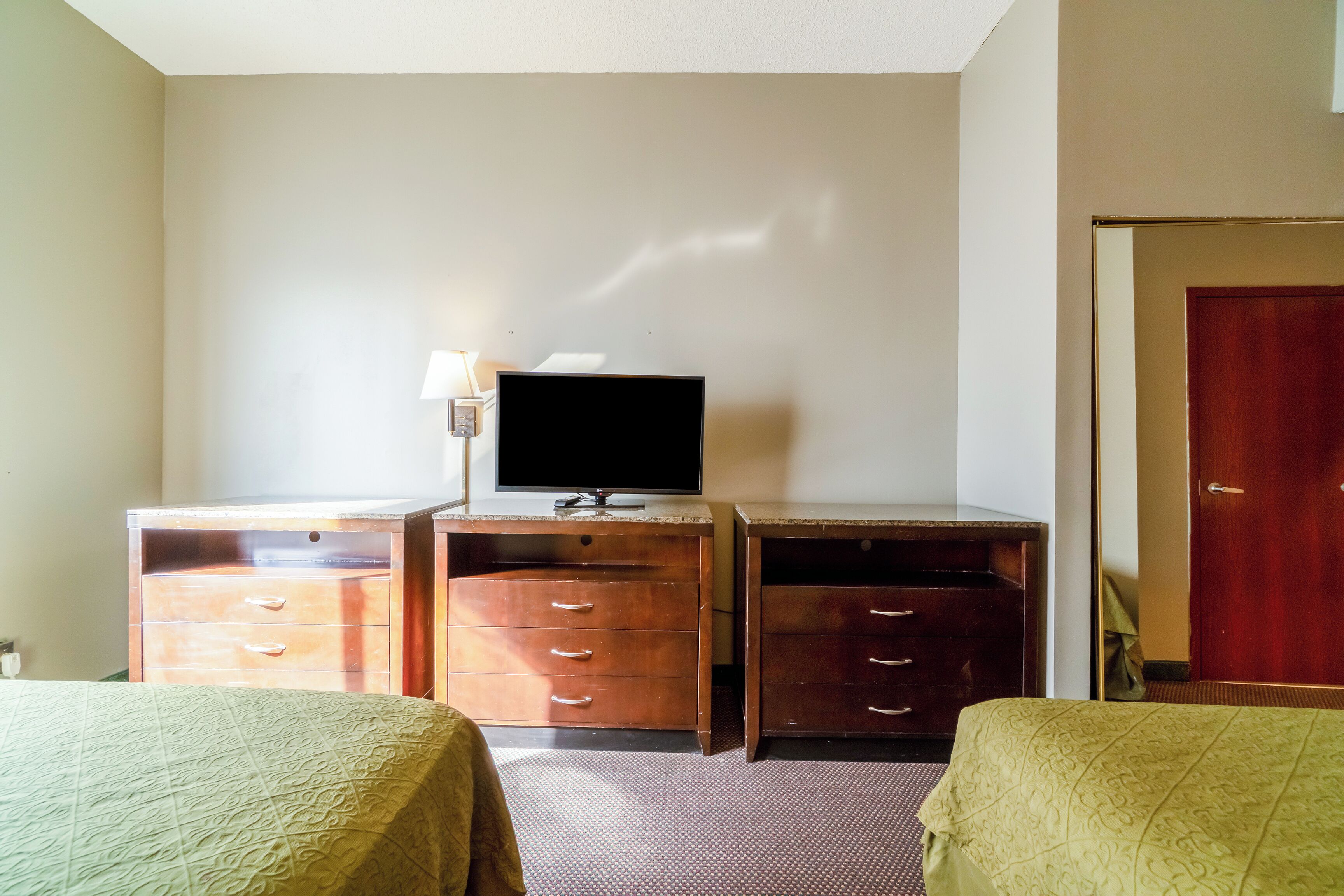 Een hotelkamer met een bed, een bureau met lades, een televisie en een deur.