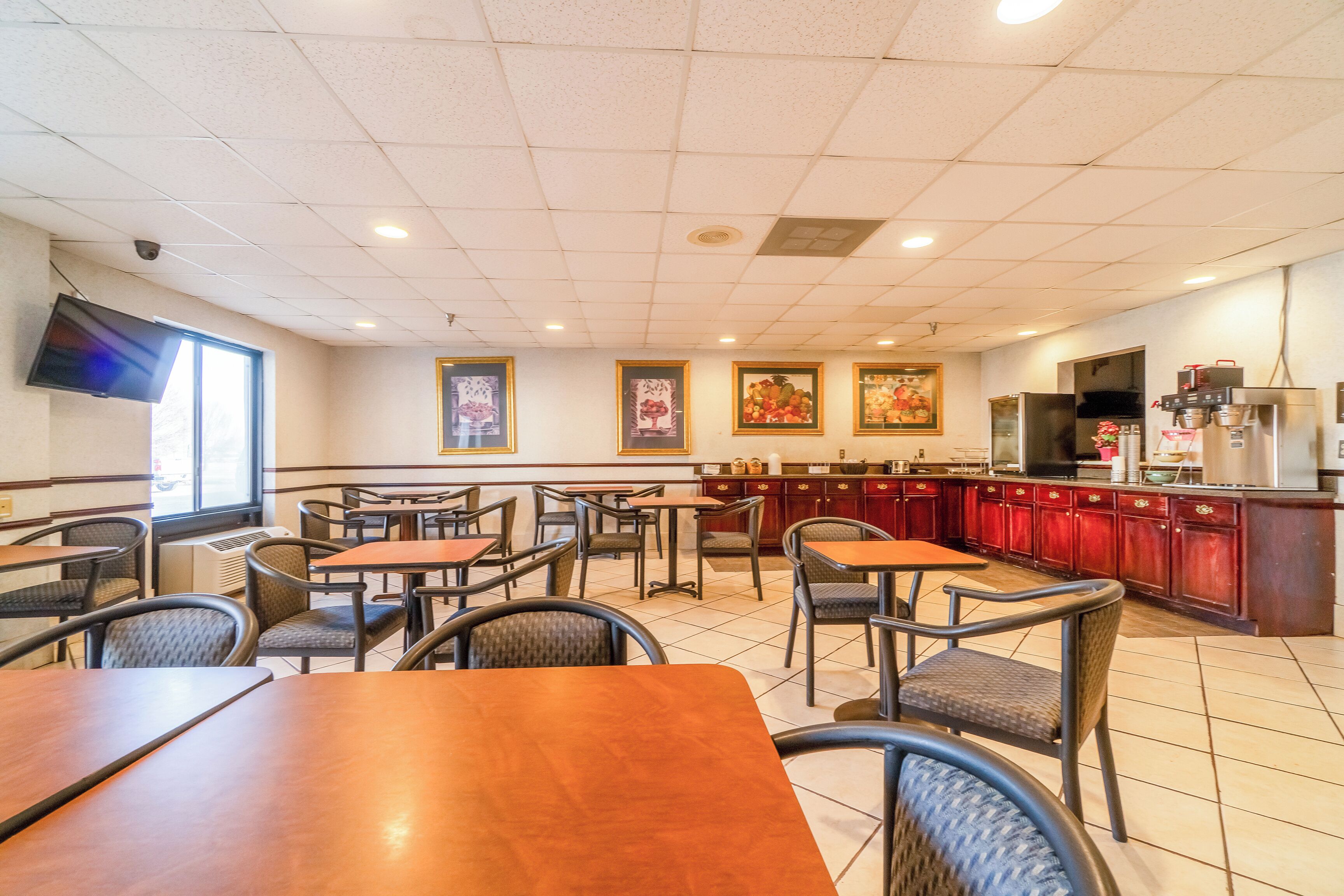 A restaurant with multiple tables and chairs, a kitchen area, and a mounted television.