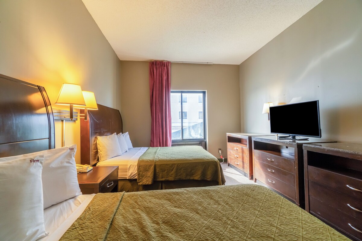 Habitación de hotel con dos camas, un escritorio, un televisor y una ventana con cortinas.