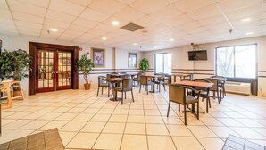 A spacious indoor area with tiled flooring, multiple tables and chairs, potted plants, and a television mounted on the wall. - Ark Suites By OYO Jonesboro I-555 (Jonesboro)
