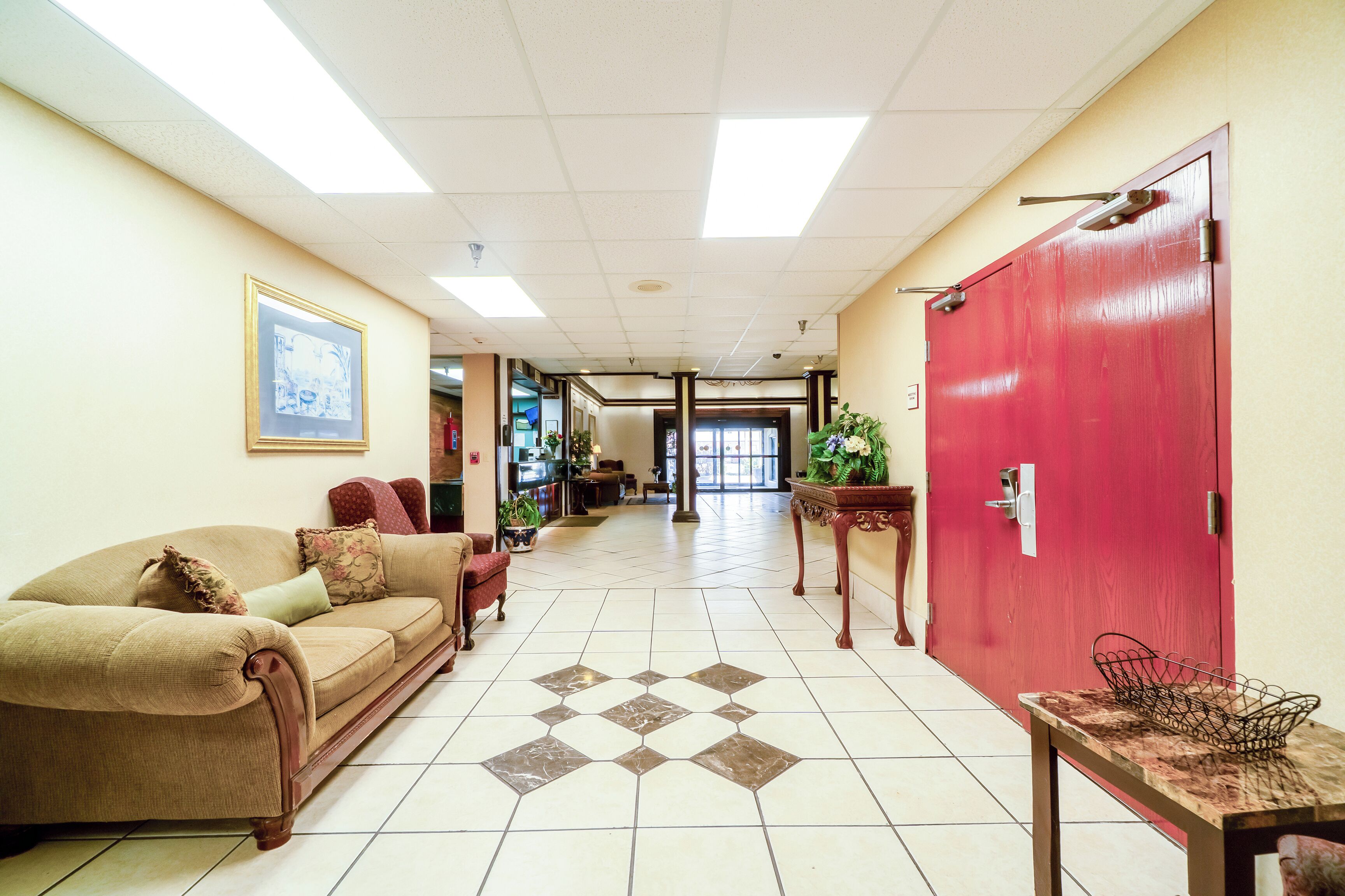 Un vestíbulo de hotel con un sofá color crema, una puerta roja y un piso de baldosas.