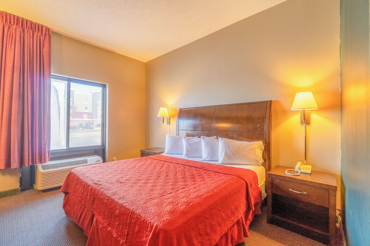 A hotel room with a large bed, two bedside lamps, a nightstand with a phone, and a window with curtains.